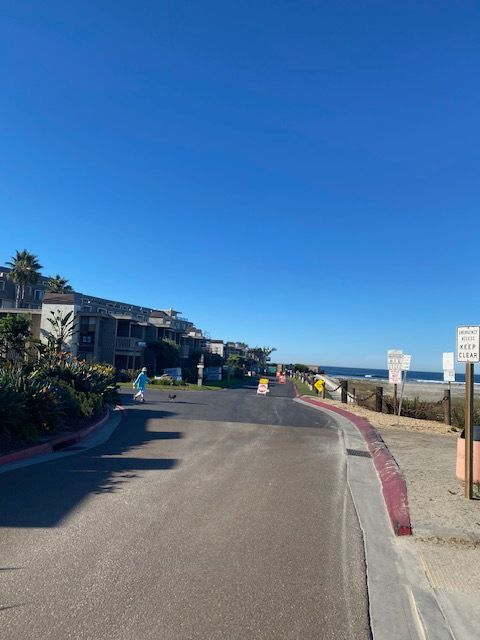 Sunny coastal road beside modern buildings and a beach under a clear blue sky