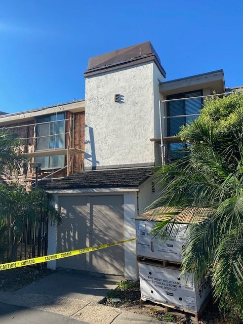 Fire-damaged townhouse with boarded lower windows and yellow caution tape under a clear blue sky