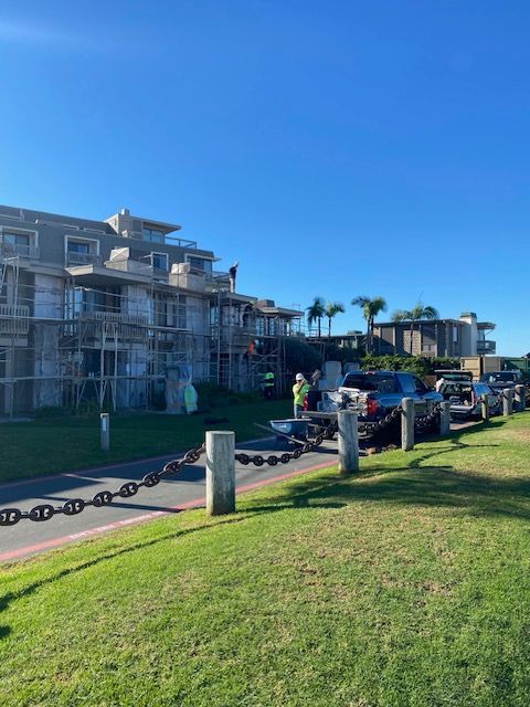 People walking and biking along a sunny waterfront path beside apartment buildings and palm trees