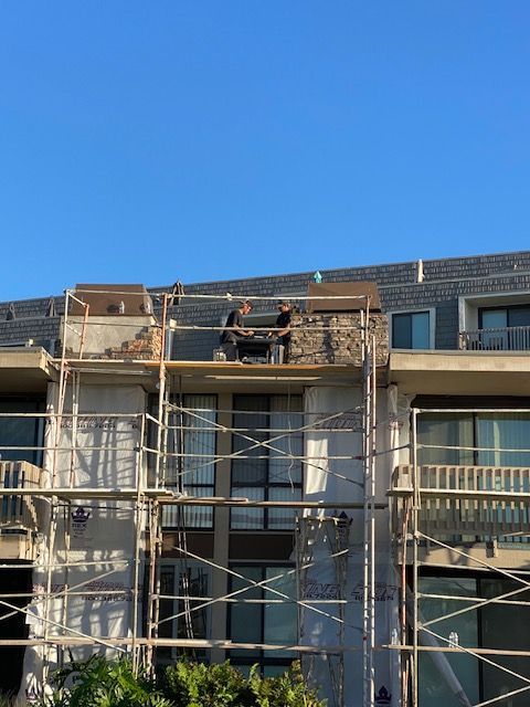 Workers on scaffolding repairing a building facade under a clear blue sky