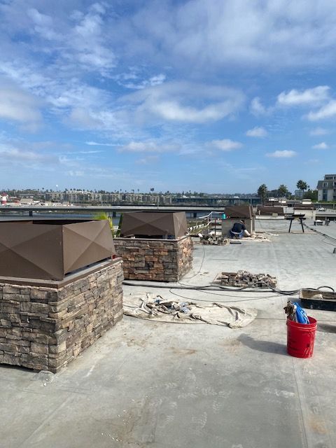 Rooftop construction site with stone columns, a red bucket, and a cloudy blue sky.