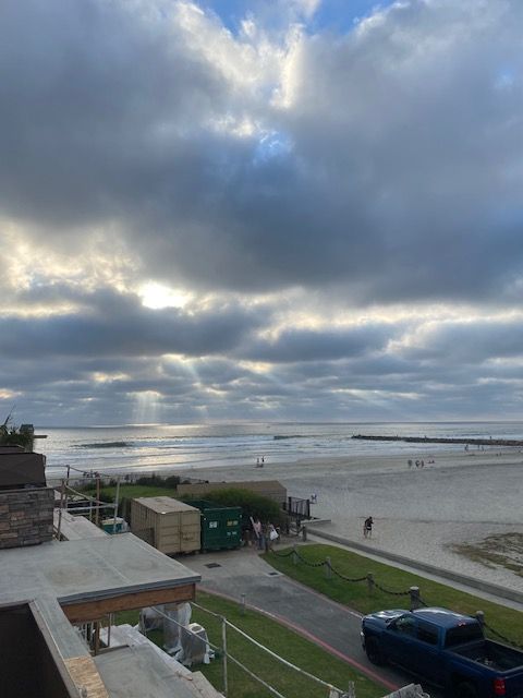 Cloudy beach scene with a wide shoreline, calm water, and a parked blue truck by a path in the foreground