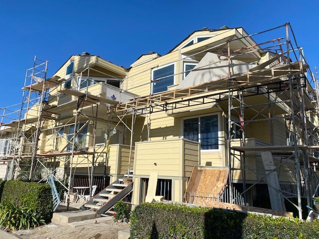Yellow house under construction with scaffolding and a ladder, viewed from the front