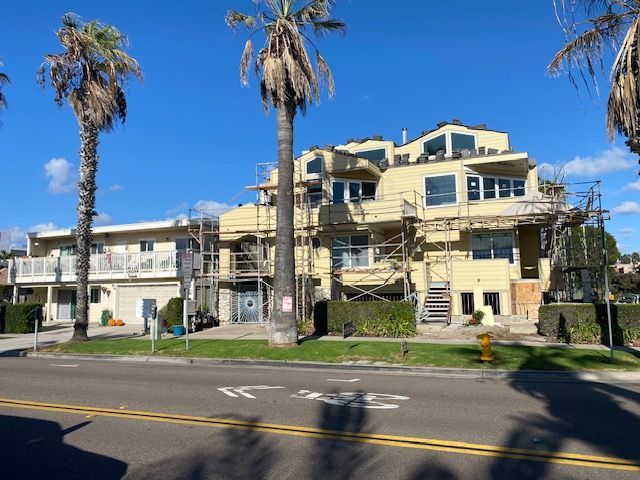 Damaged beige apartment building with palm trees beside a road under a blue sky