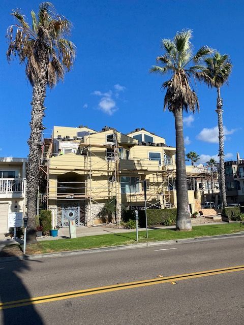 Palm trees beside a beige apartment building under construction on a sunny street.