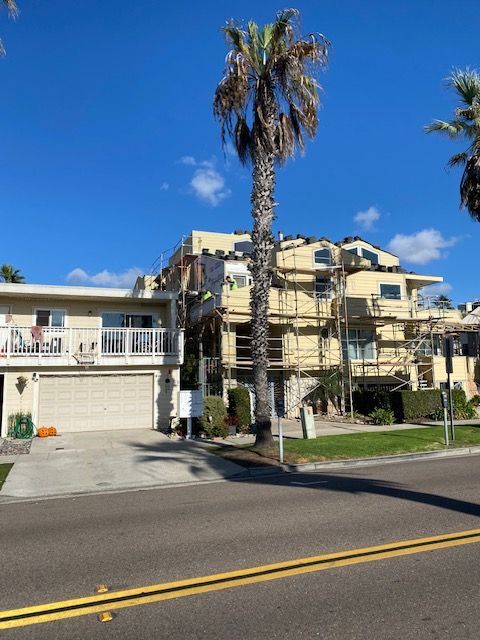 Apartment building with palm trees and balconies on a sunny street, viewed from across the road