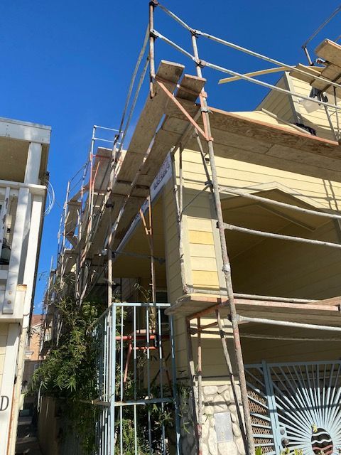 Yellow building with scaffolding under a clear blue sky, viewed from a narrow street