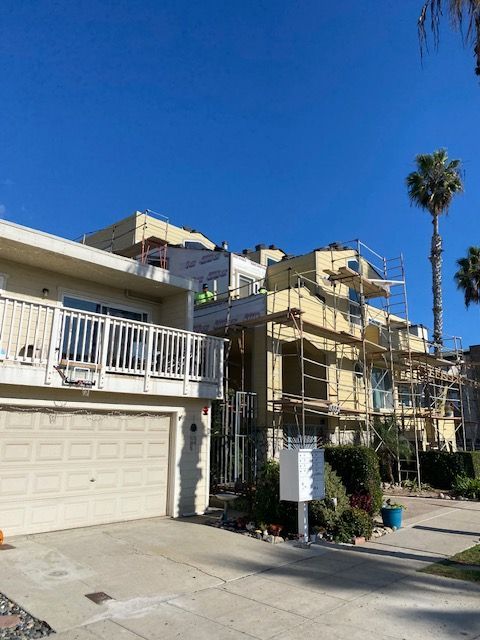 Residential street with beige townhouses, a garage, scaffolding, and a tall palm tree under a clear blue sky