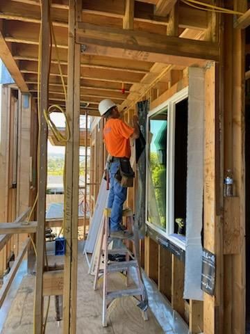 Worker on ladder installing wiring inside a wooden building under construction.