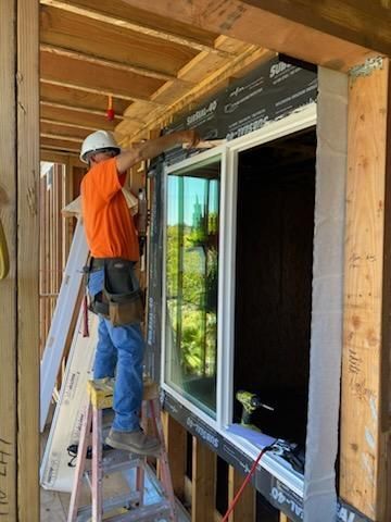 Worker on ladder installing a large sliding glass door in a framed porch opening.
