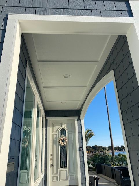 Modern white front porch with decorative glass door and gray siding under a bright blue sky