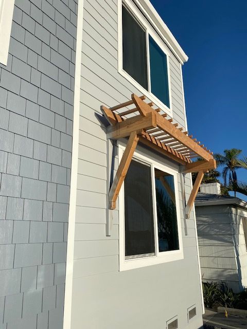Wall-mounted wooden awning over a second-story window on a gray house exterior.