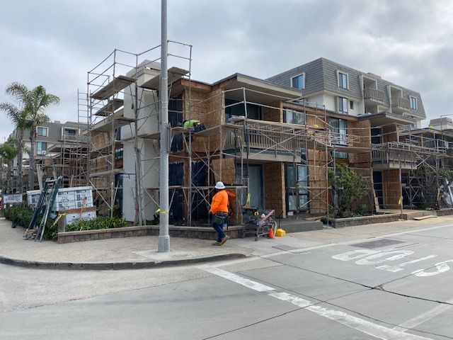 Construction workers on scaffolding outside a gray apartment building on a street corner.