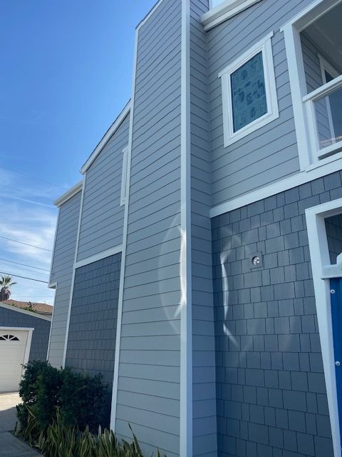 Gray two-story townhouse exterior with white trim and blue shingles under a clear sky