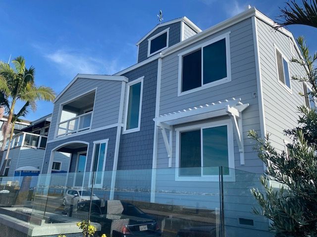 Gray beach house with white trim and large windows beside a glass fence under a blue sky