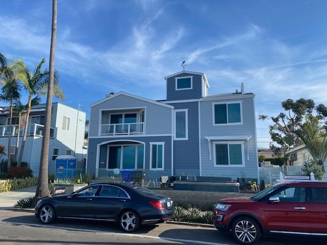 Blue seaside house with balconies and parked cars under a bright sky