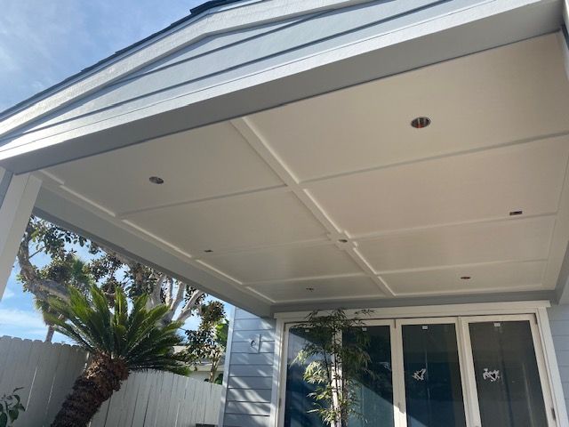 Modern home exterior with a covered patio, white ceiling, glass doors, and palm tree beside a fence