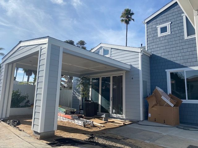Partially built white patio addition beside a blue house, with construction debris and boxes nearby.