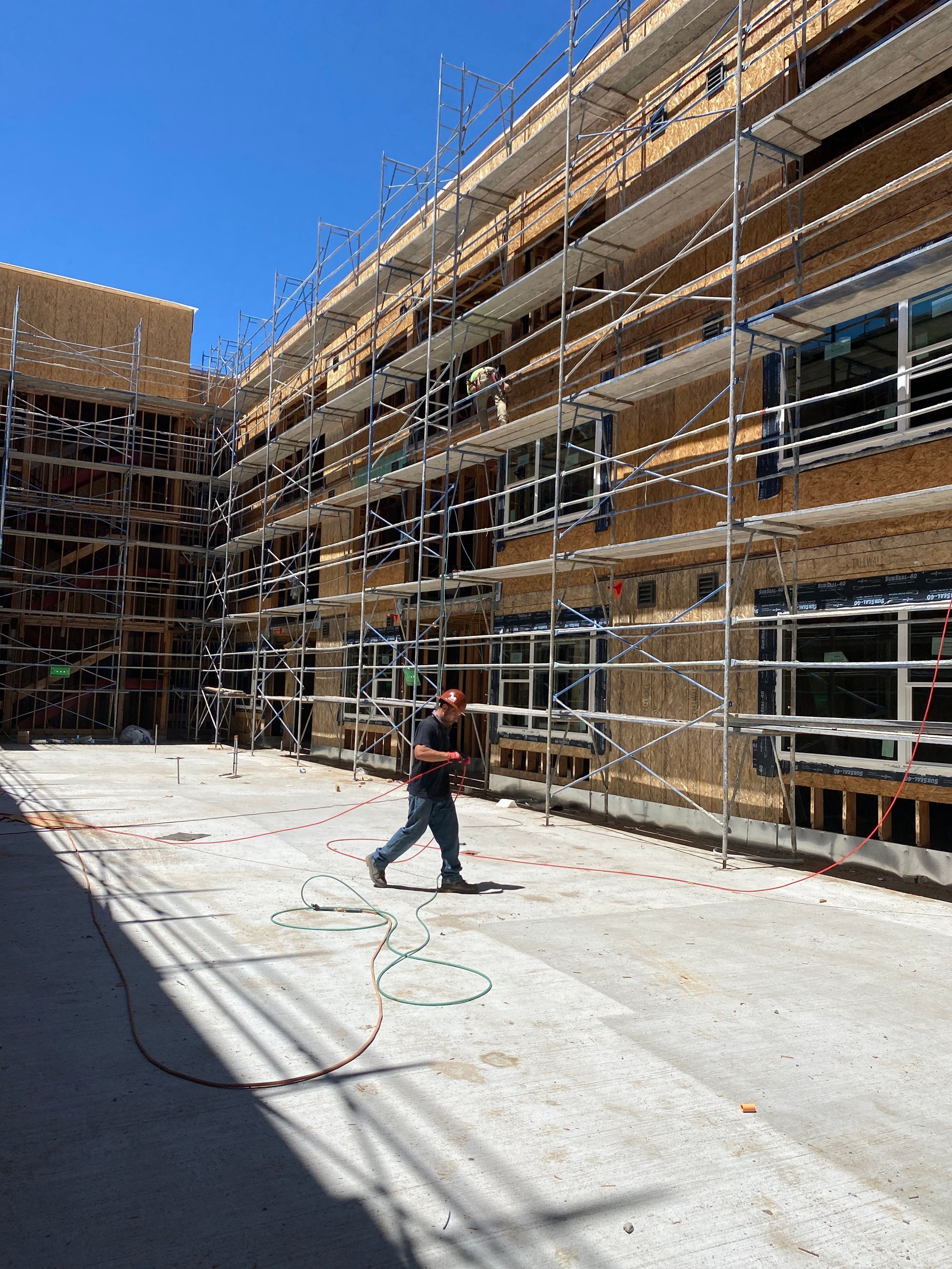 Construction site with scaffolding around a building and a worker walking across a concrete courtyard.