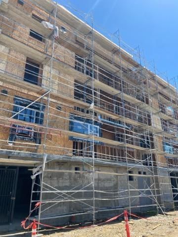 Brick building under renovation with scaffolding and netting against a blue sky