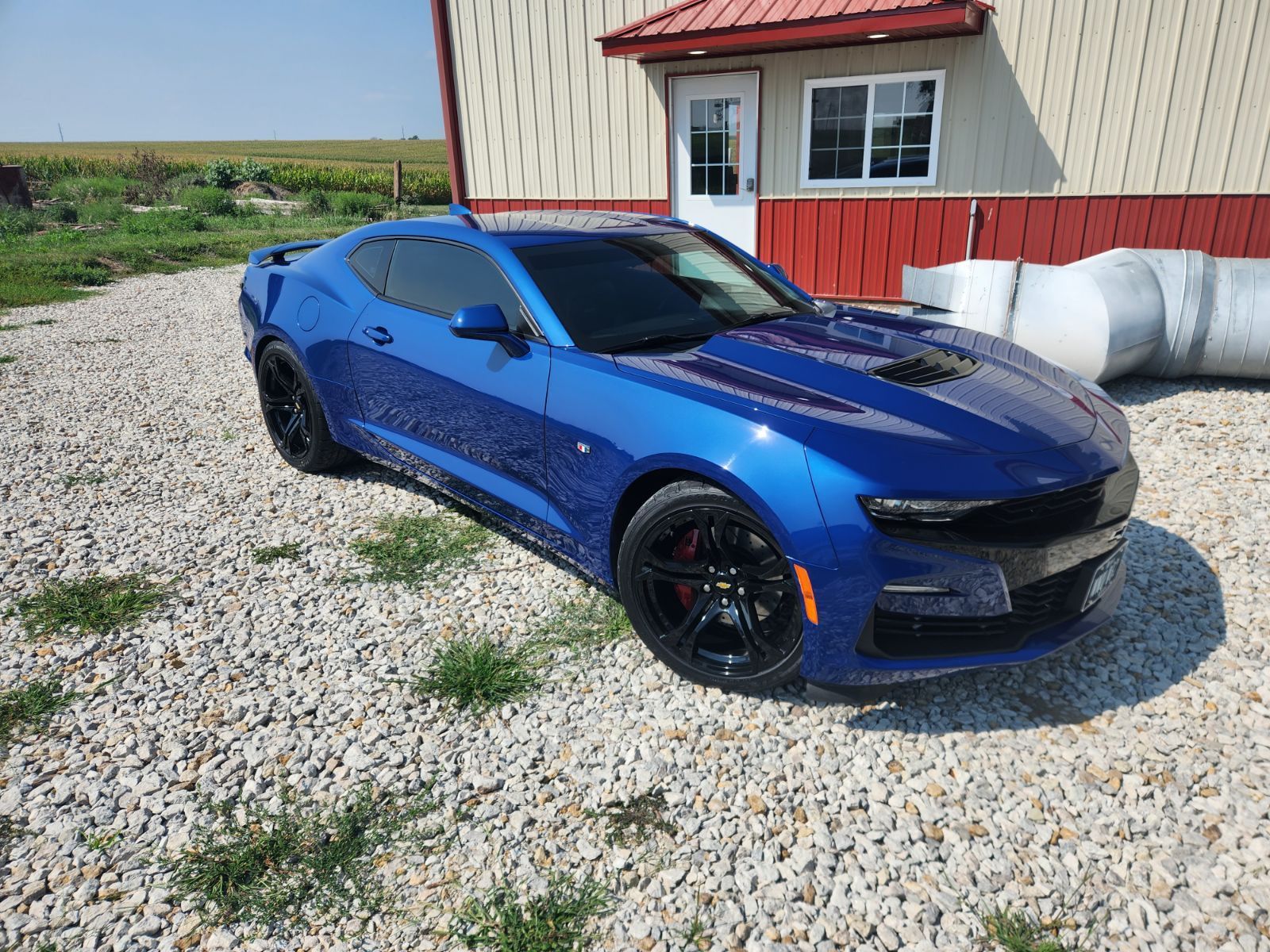 A blue chevrolet camaro is parked in a gravel lot in front of a building.