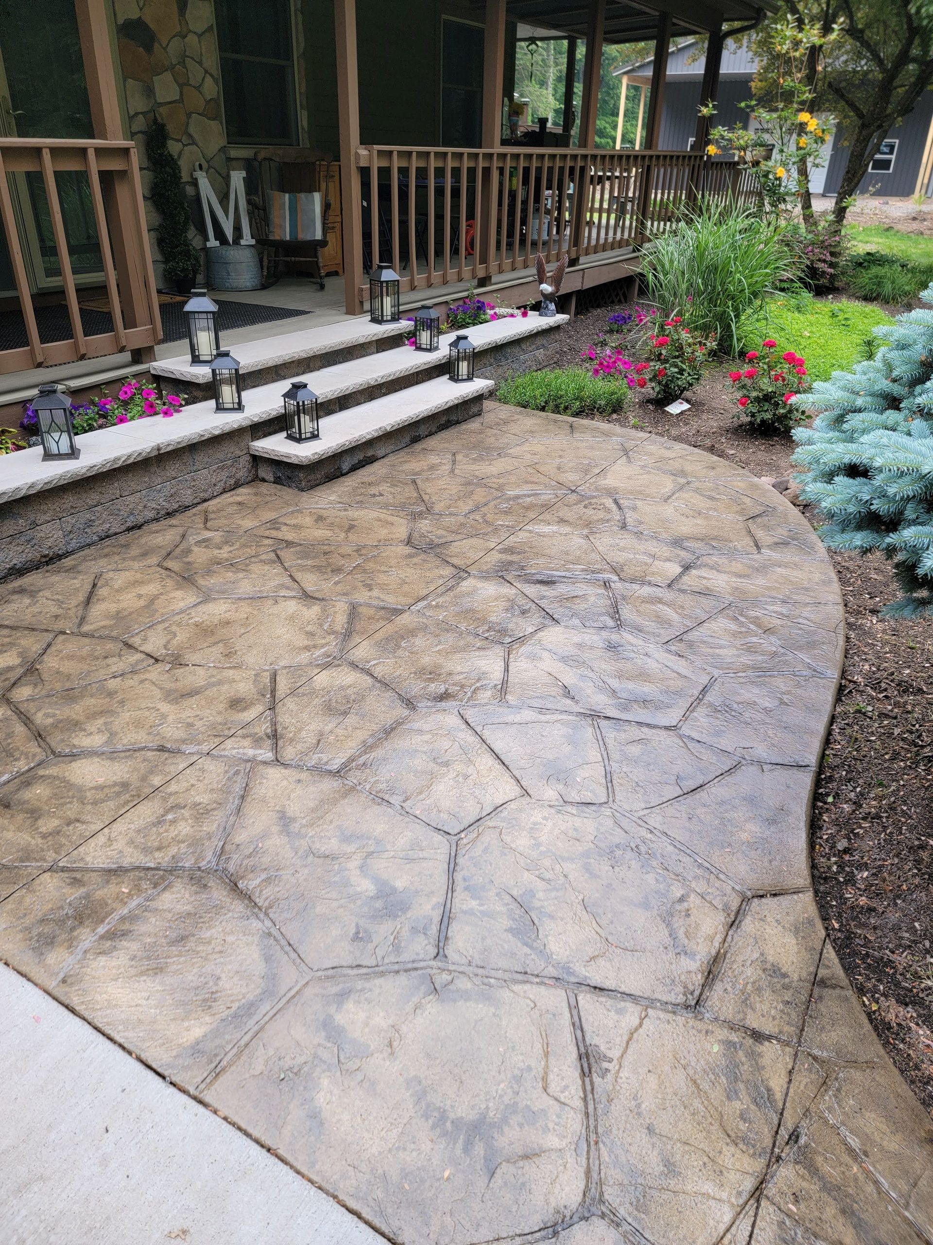 Stamped concrete patio and steps leading to a porch, with landscaping and lanterns.