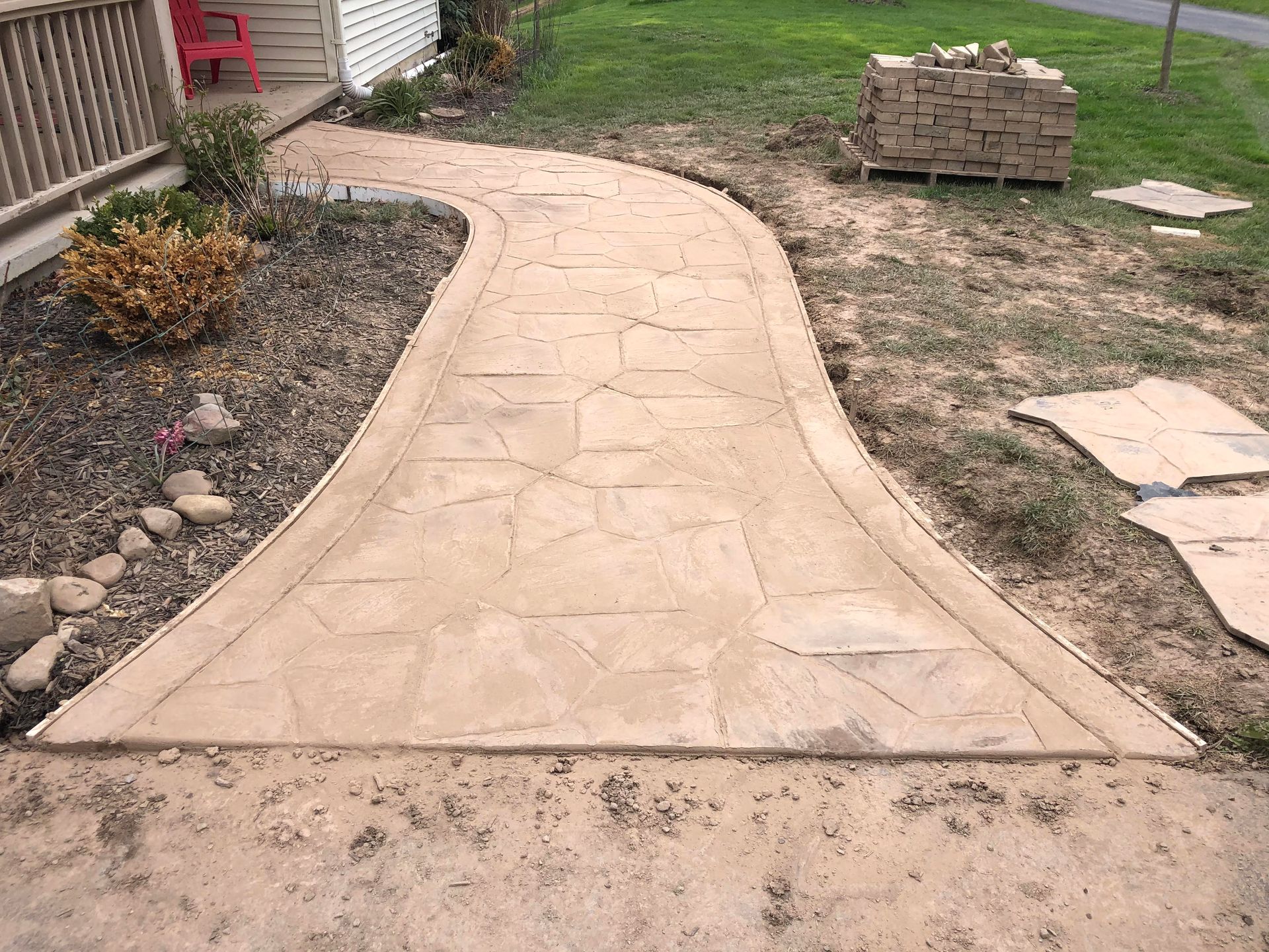 Stamped concrete pathway winding from a driveway to a porch. Brown color with stone pattern.