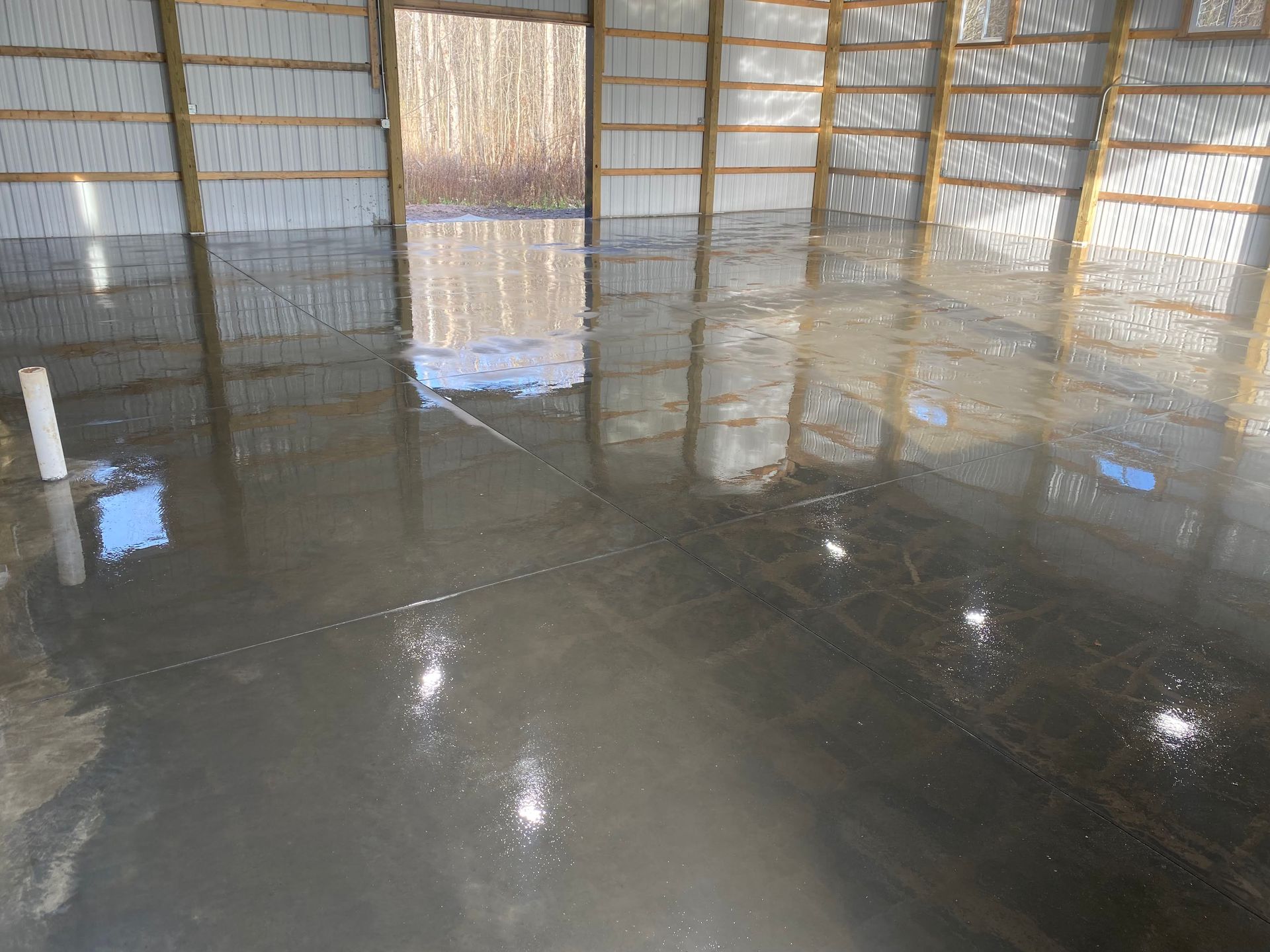 Wet, freshly poured concrete floor inside a wooden framed building, reflecting light.