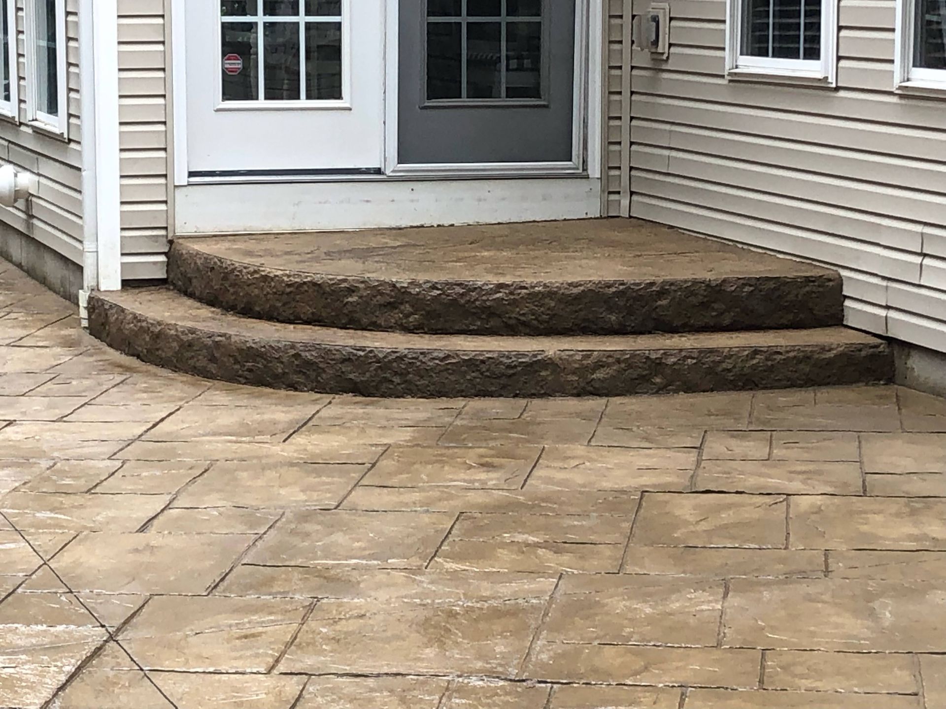 Two brown stone steps lead to a doorway, with a matching stone patio below.