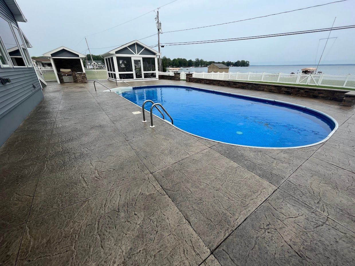 Pool with blue water and stamped concrete patio next to a lake, with gazebos.