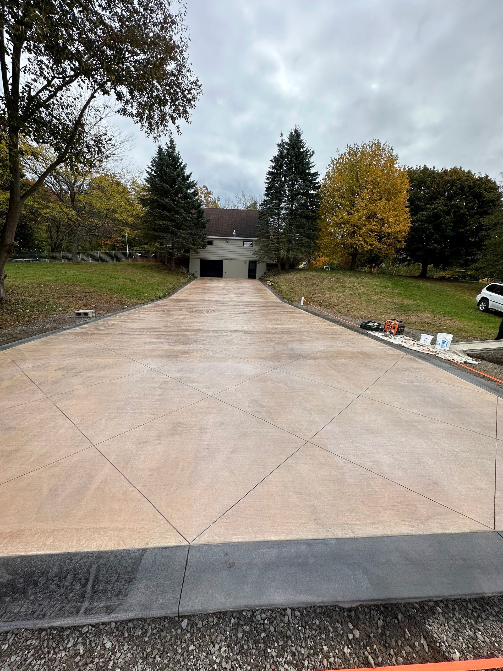 A new concrete driveway with cut lines leads to a house with a garage under an overcast sky.