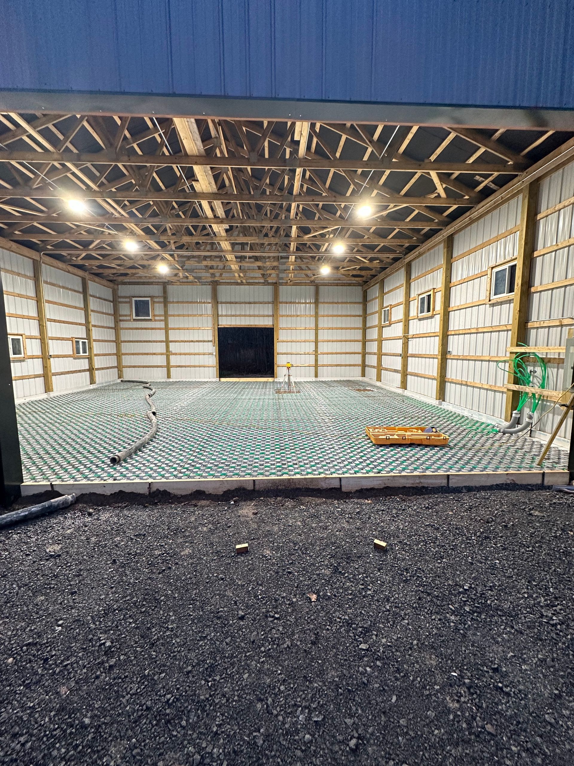 Interior of a building under construction, showing a grid of green pipes on a concrete floor.