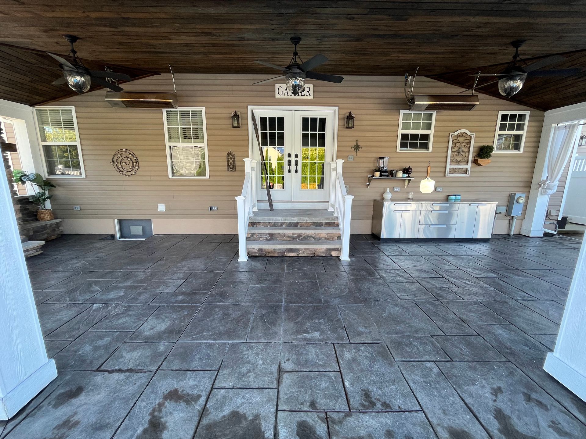 Covered patio with stamped concrete floor, outdoor kitchen, and white French doors.