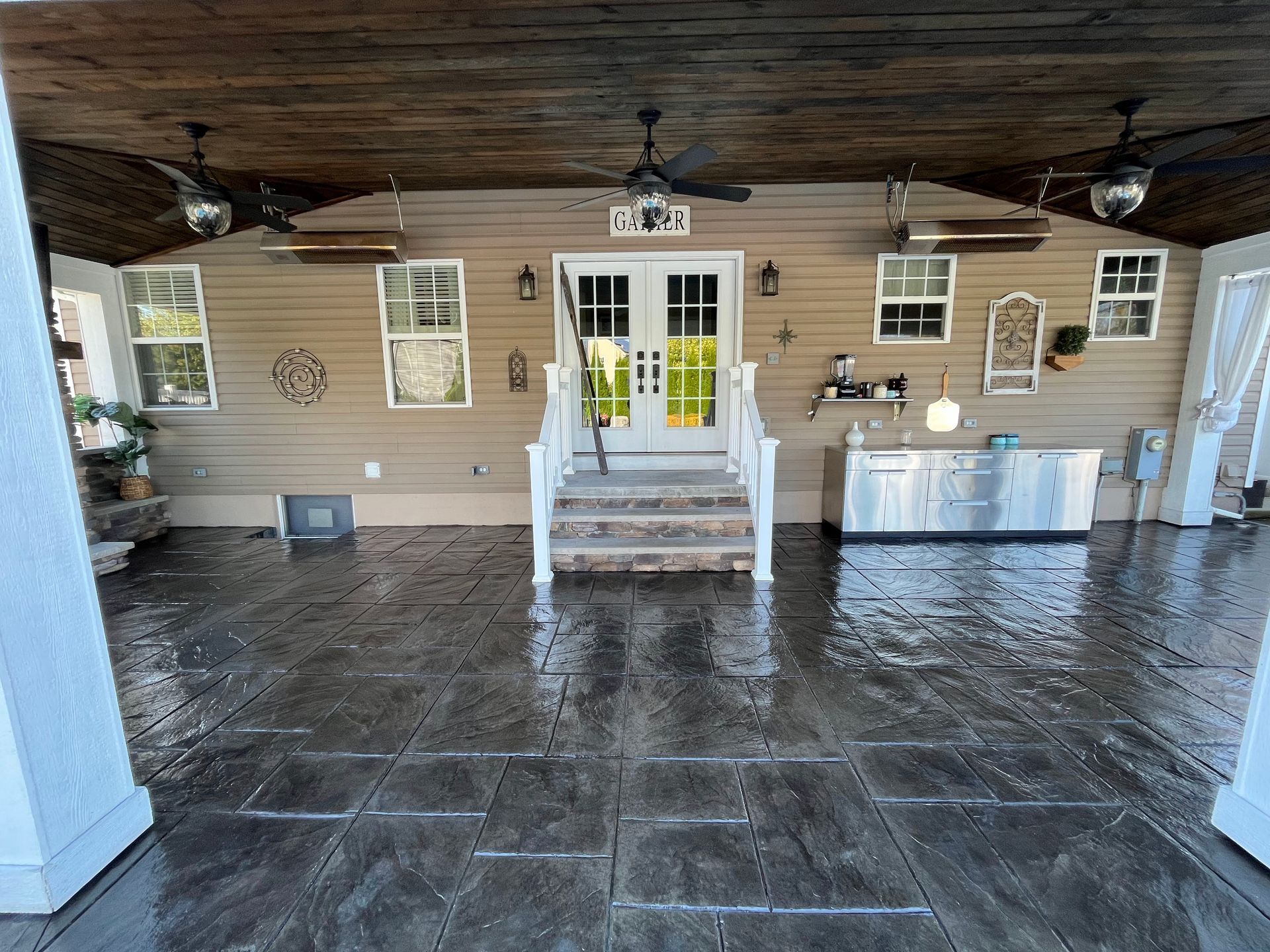 Covered patio with dark gray tiled floor, white doors, and ceiling fans.
