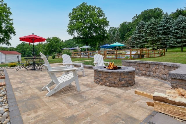 Patio with white Adirondack chairs, red umbrella, and stone fire pit in a landscaped backyard