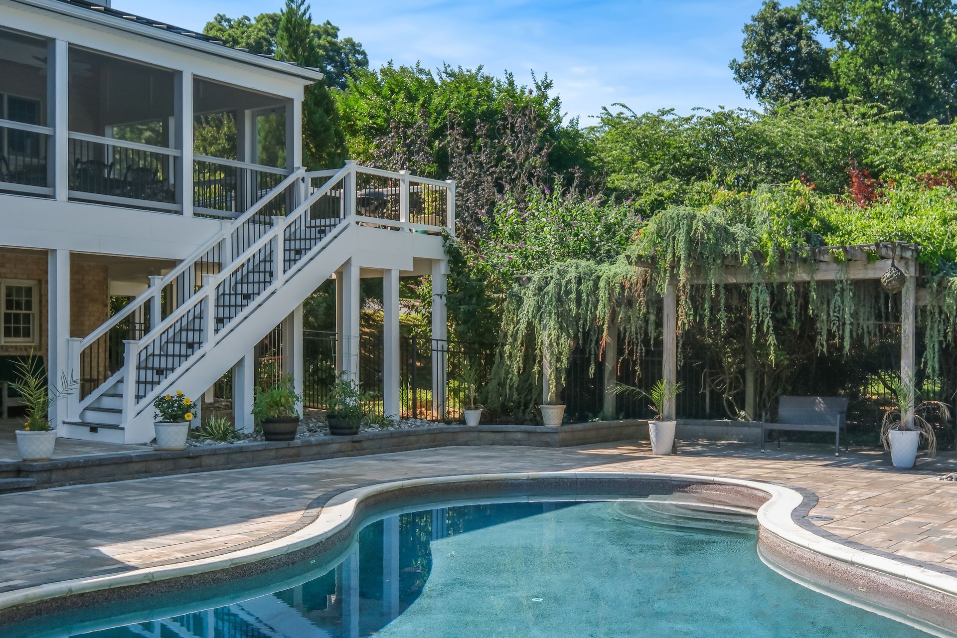 Backyard pool beside a house with white stairs and lush tropical landscaping
