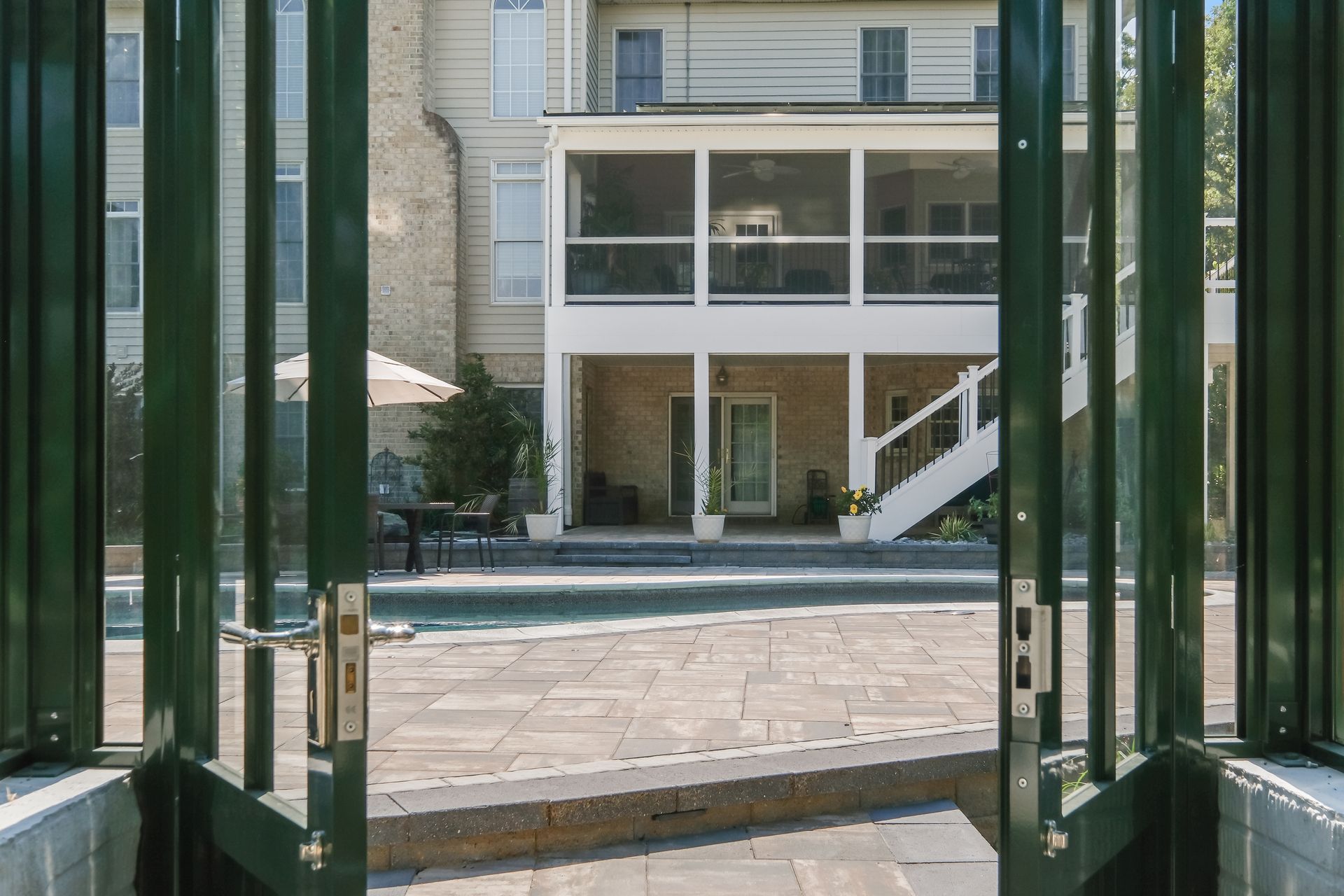 View through green doors to a sunny courtyard and modern building with large windows