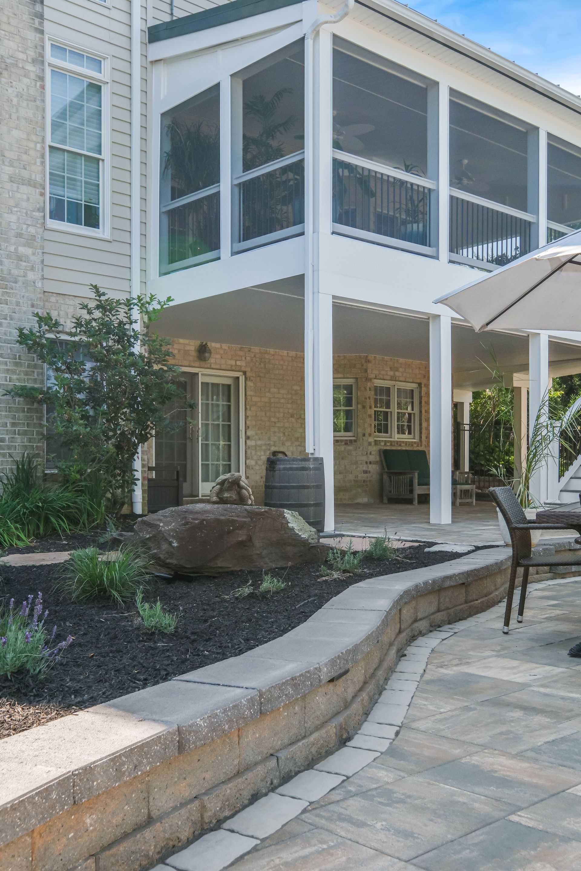Patio with stone walkway, screened porch, white columns, and landscaped garden beds beside a house