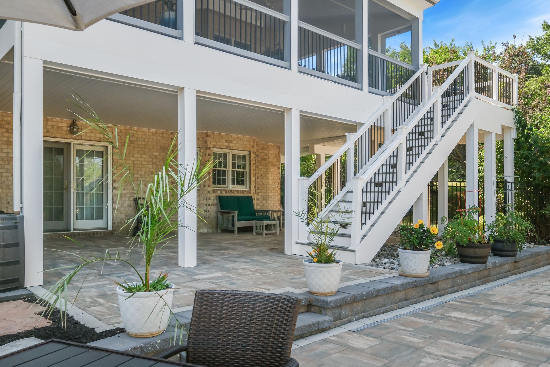 Covered patio with white staircase, wicker seating, and potted plants outside a house