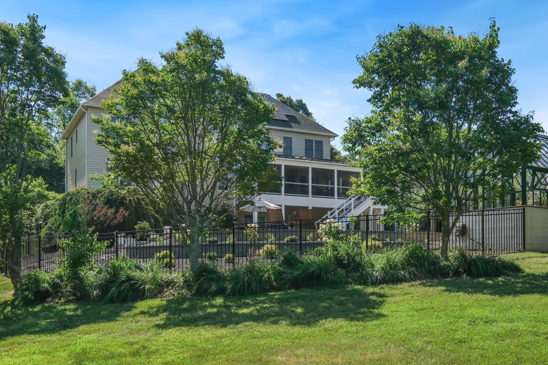 Large gray house behind trees and garden under a bright blue sky