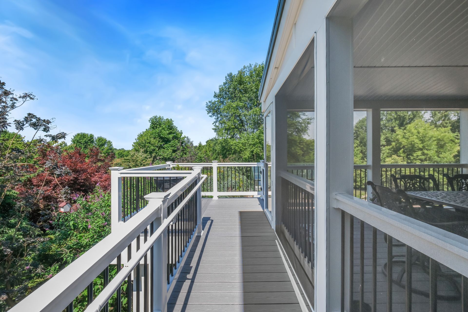 Outdoor walkway with gray railings beside a modern building, overlooking green trees under a blue sky