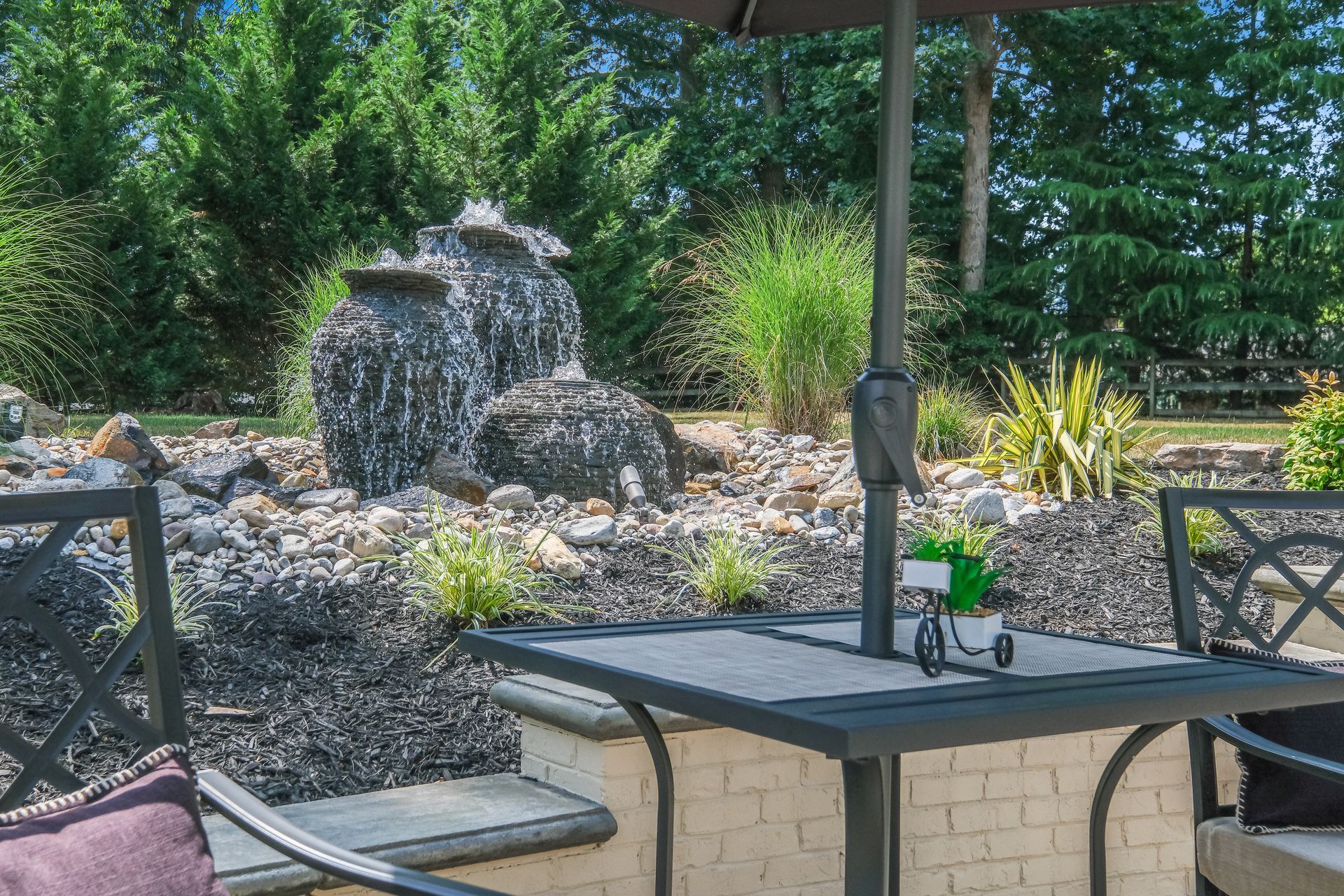 Patio table and chairs overlooking a small rock waterfall and greenery outdoors
