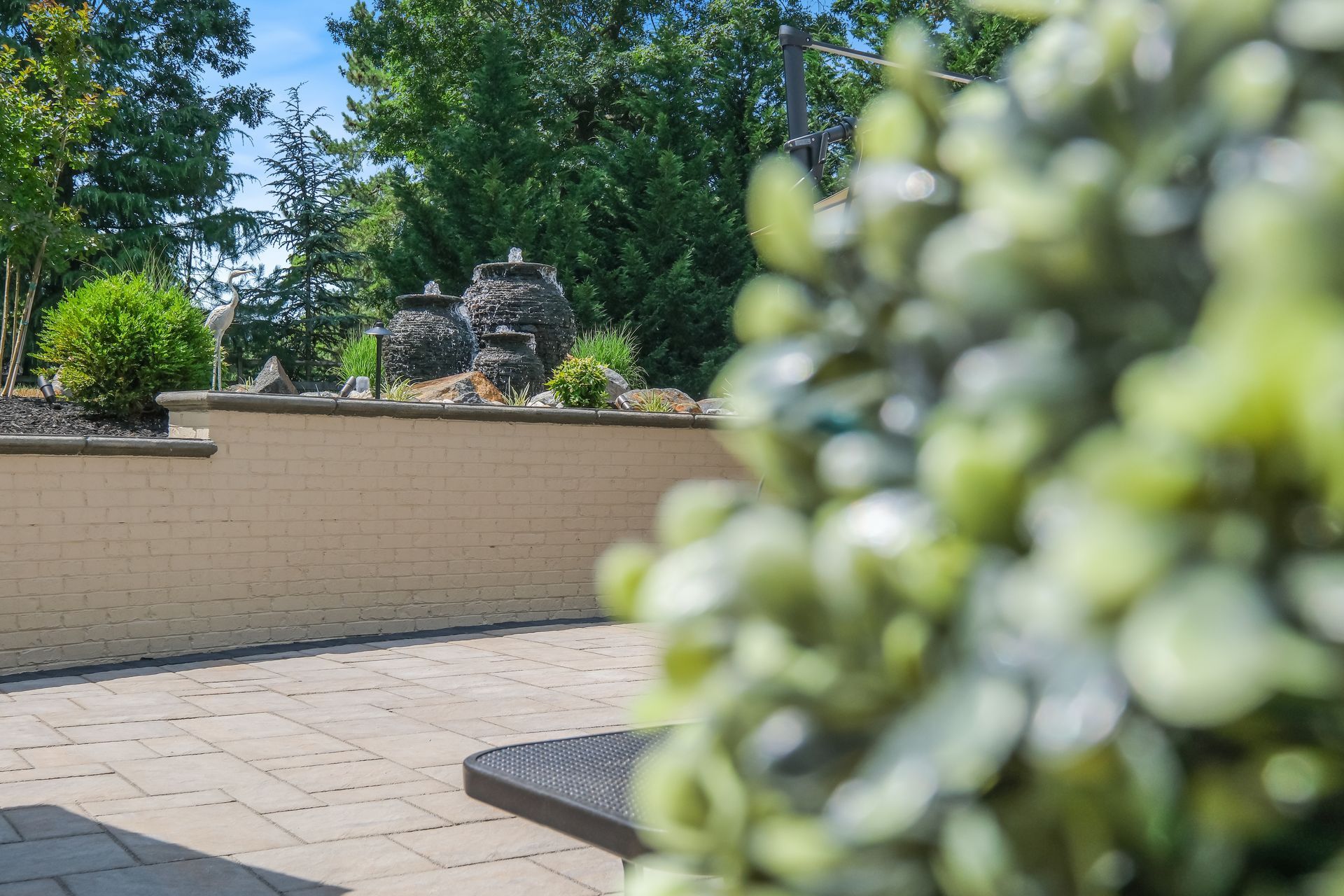 Sunny patio with stone paving, cream wall, trees, and blurred green flowers in the foreground