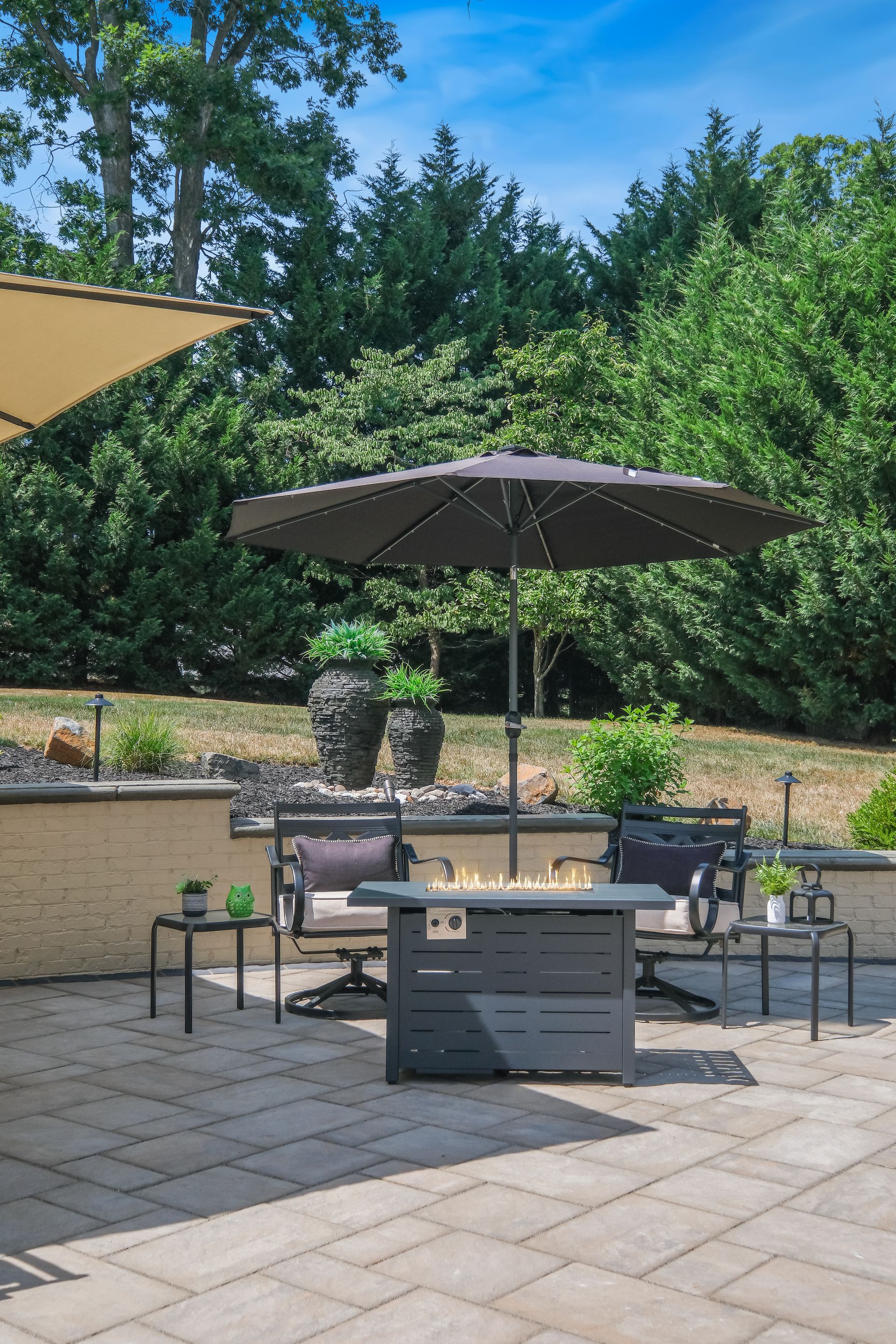 Patio seating area with umbrella, fire pit, and potted plants in a sunny garden