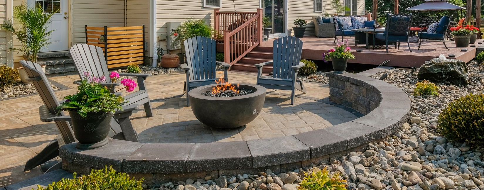 Circular stone patio with planters and blue chairs in a landscaped backyard garden