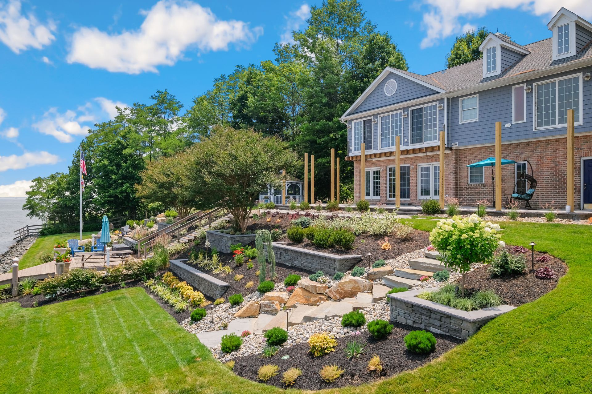 Landscaped front yard with stone terraced garden beside a gray house and blue sky