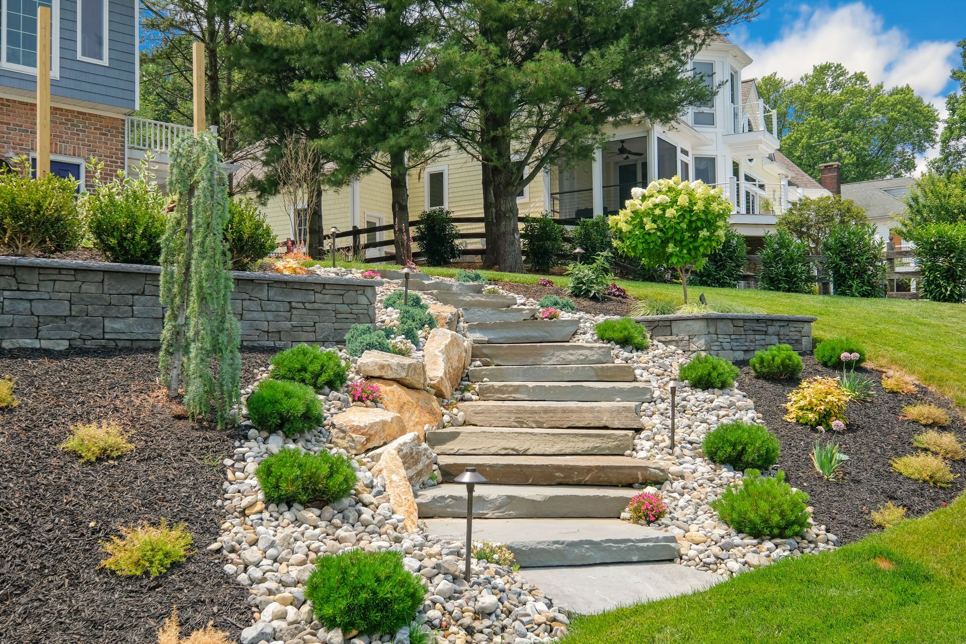 Landscaped stone steps with rocks, shrubs, and mulch leading up to a modern house