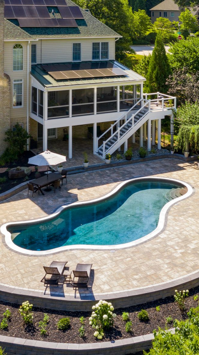 Backyard pool with lounge chairs beside a glass greenhouse and trees in the background