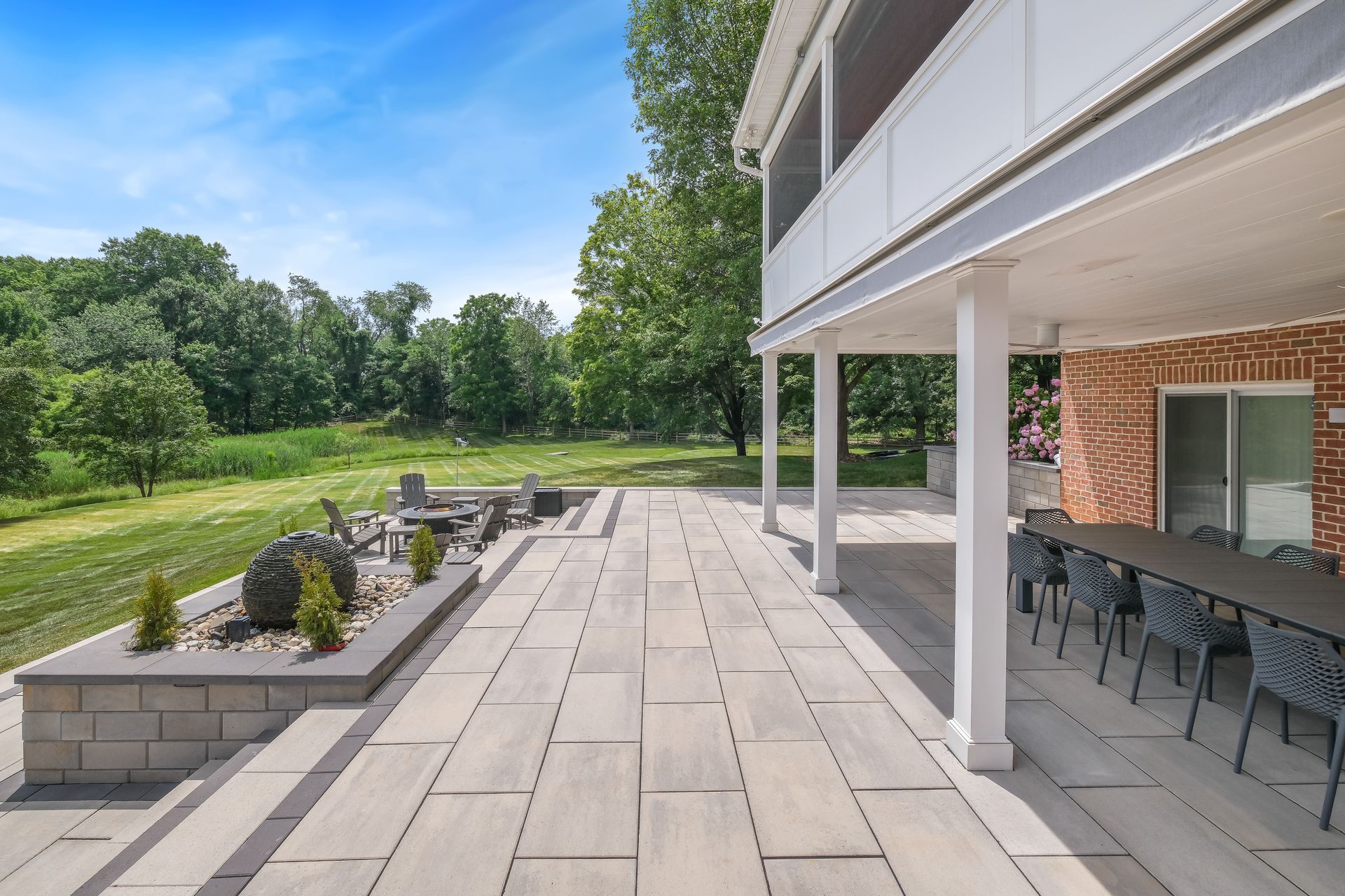 Modern patio with stone pavers, outdoor seating, and a landscaped lawn beside a house