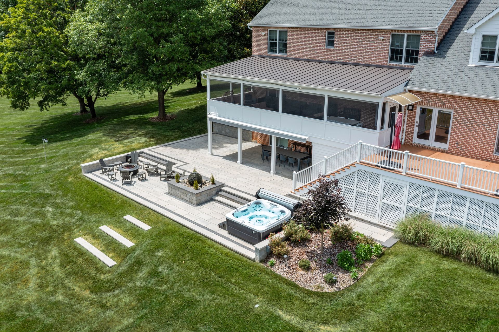 Backyard deck with a hot tub, patio furniture, and a brick house with an American flag